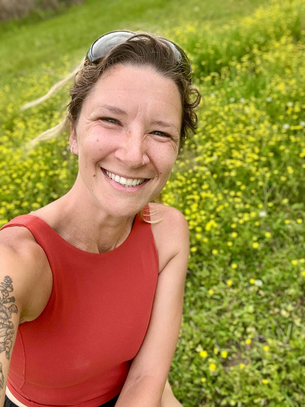 Woman in a red sleeveless top sitting in a field of yellow flowers.