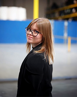 Woman wearing glasses and a black jacket in an industrial setting